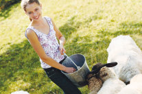 Mädchen steht mit Eimer vor Schafen