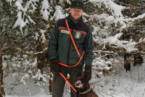 Michael Bug steht mit Hund vor schneebedeckten Nadelbäumen