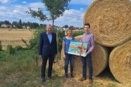 3 Personen stehen von Stroh-Rundballen, 2 davon halten ein Schild