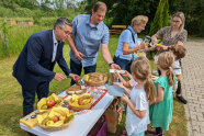 Erwachsene und Kinder stehen um Tisch mit Speisen