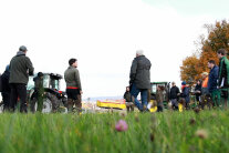 Personen stehen auf einer Wiese vor landwirtschaftlichen Geräten